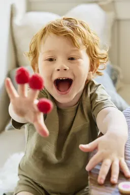 Smiling boy wearing sustainable clothing with raspberries on his fingers