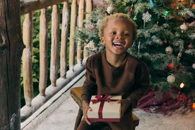 Toddler Holding gift in front of Christmas tree
